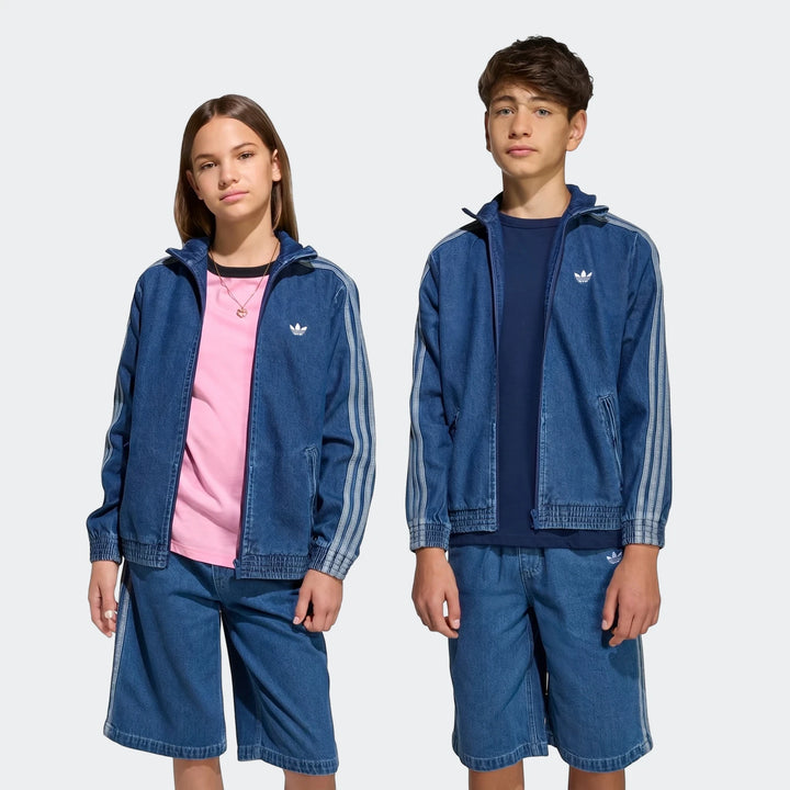Two young models, a girl and a boy, wearing matching blue Adidas Firebird Denim Track Tops and coordinating shorts,