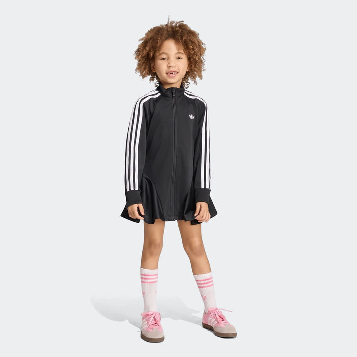 Young girl wearing a black Adidas Firebird Longsleeve Dress with white stripes, white socks, and pink shoes, full length