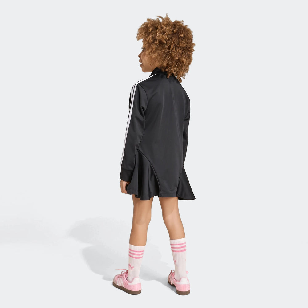 Girl in black Adidas Firebird Longsleeve Dress with white stripes, pink sneakers, and white socks, viewed from the back.