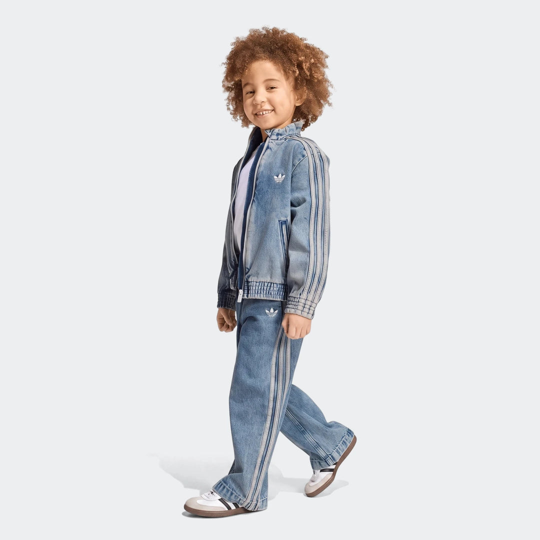 Smiling child wearing an Adidas Firebird Loose Denim Track Jacket and matching Track Pants, walking sideways on a white