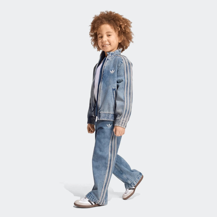 Smiling child wearing an Adidas Firebird Loose Denim Track Jacket and matching Track Pants, walking sideways on a white