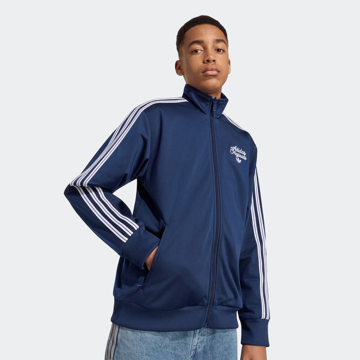 Young male model wearing a navy blue Adidas Firebird Loose Reversible Tracktop with white stripes and Adidas Originals logo.