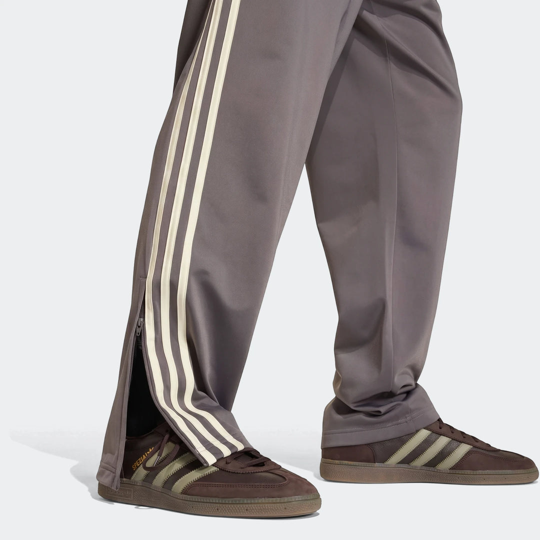 Gray Adidas Firebird Track Pants with cream three stripes on the side, worn by a person paired with brown Adidas Spezial