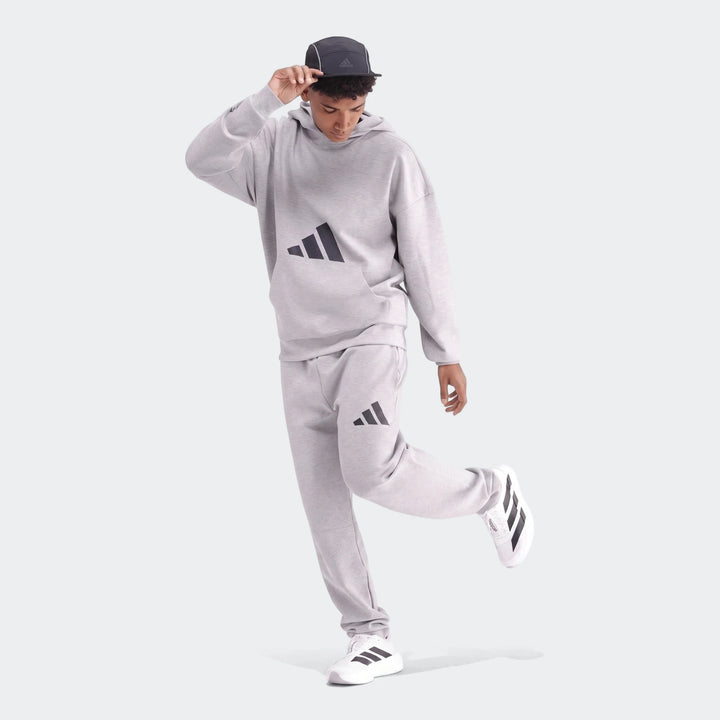 Young man wearing a light gray Adidas Future Icons 3-Bar Hoodie and matching sweatpants with white sneakers.