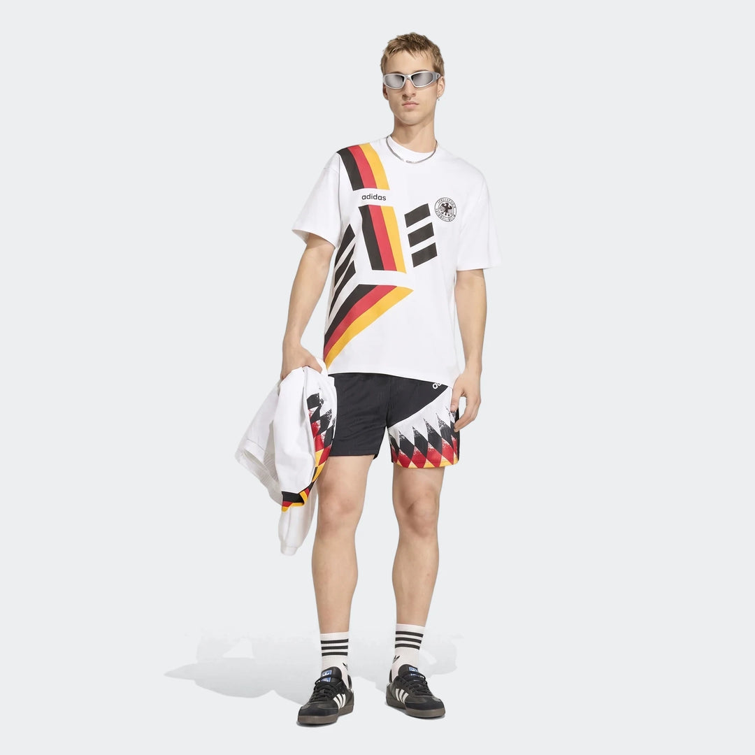 Male model wearing a white Adidas Germany T-Shirt 1994 with black, red, and yellow accents, paired with black patterned