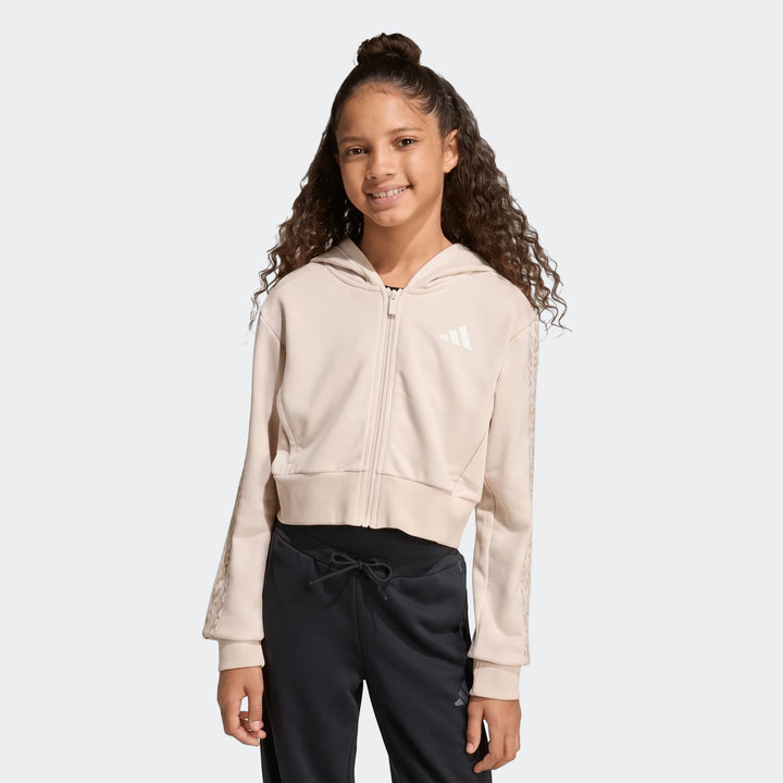 Young girl smiling, wearing an adidas Angled 3-Stripes French Terry Full-Zip Hoodie in beige and black track pants.