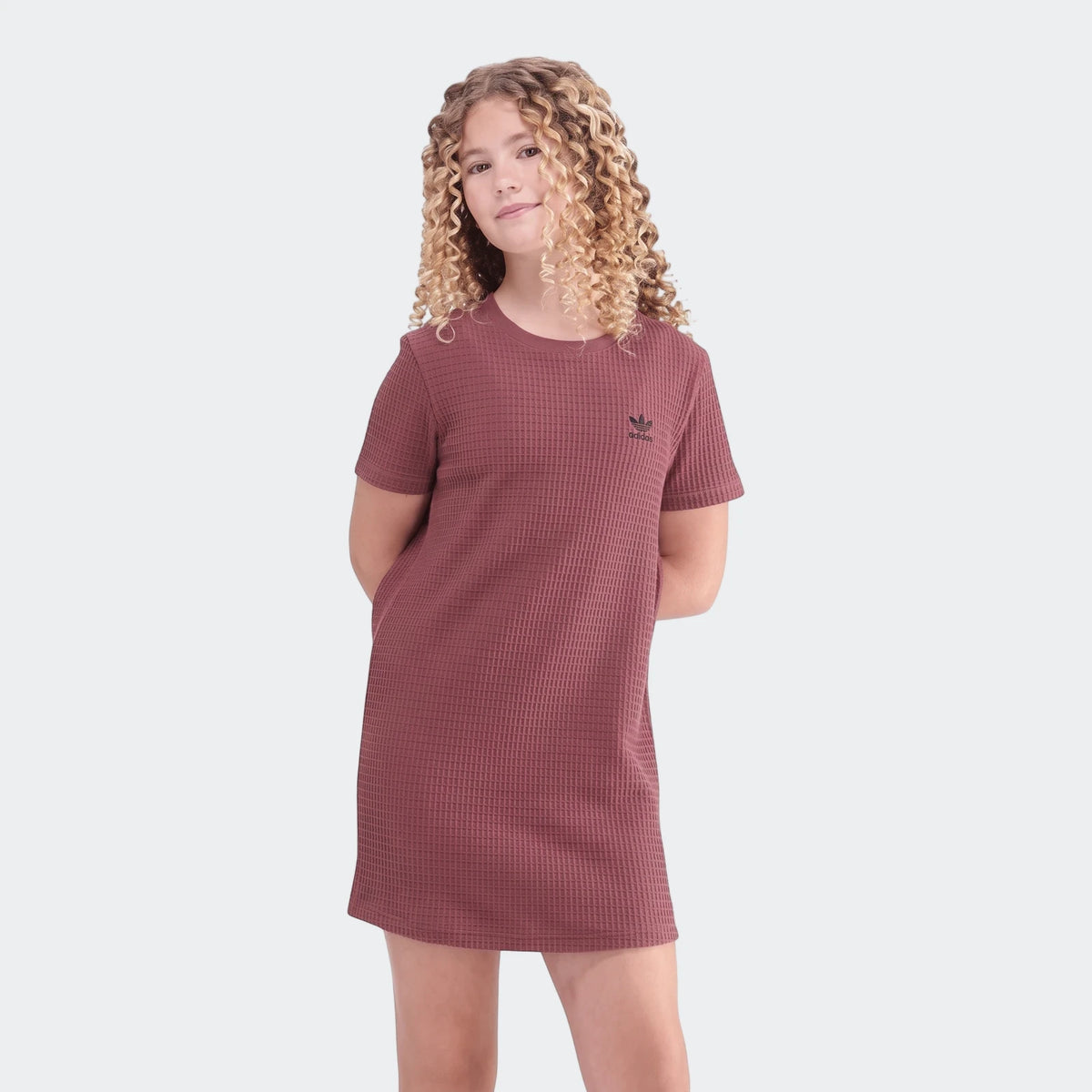 Young girl models a dark pink Adidas short-sleeve waffle dress, standing full body on a white background.