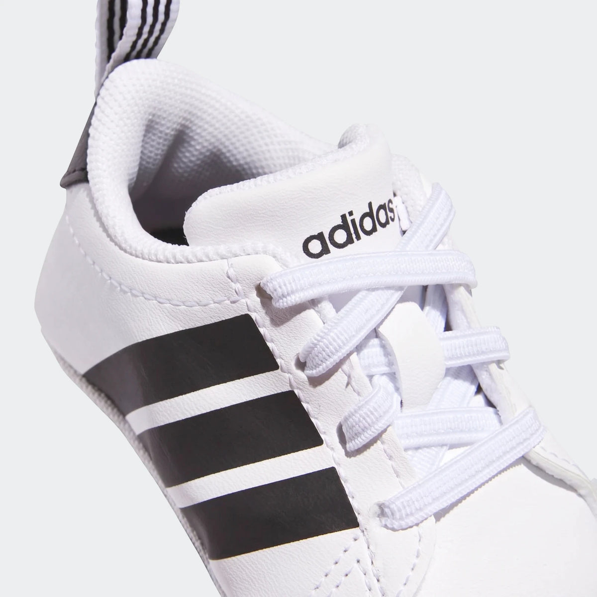 Close-up of a white Adidas Grand Court Crib baby shoe with black stripes and white laces, shown from the upper front.