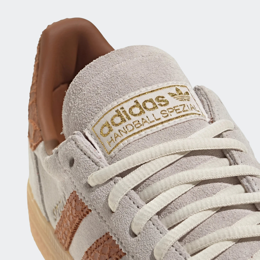 Close-up view of an Adidas Handball Spezial sneaker in light gray suede with white laces and a gold logo on the tongue,