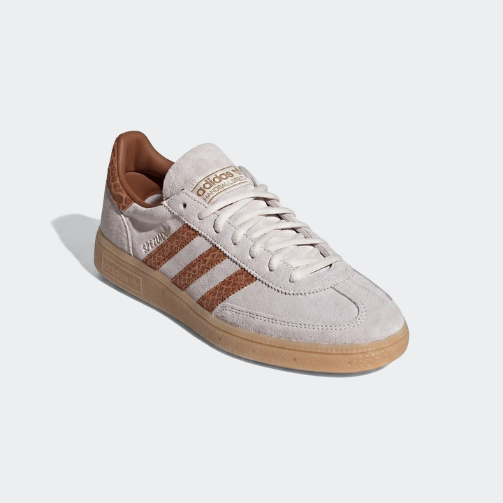 Adidas Handball Spezial sneaker in white suede with brown textured stripes and gum sole, angled side view.