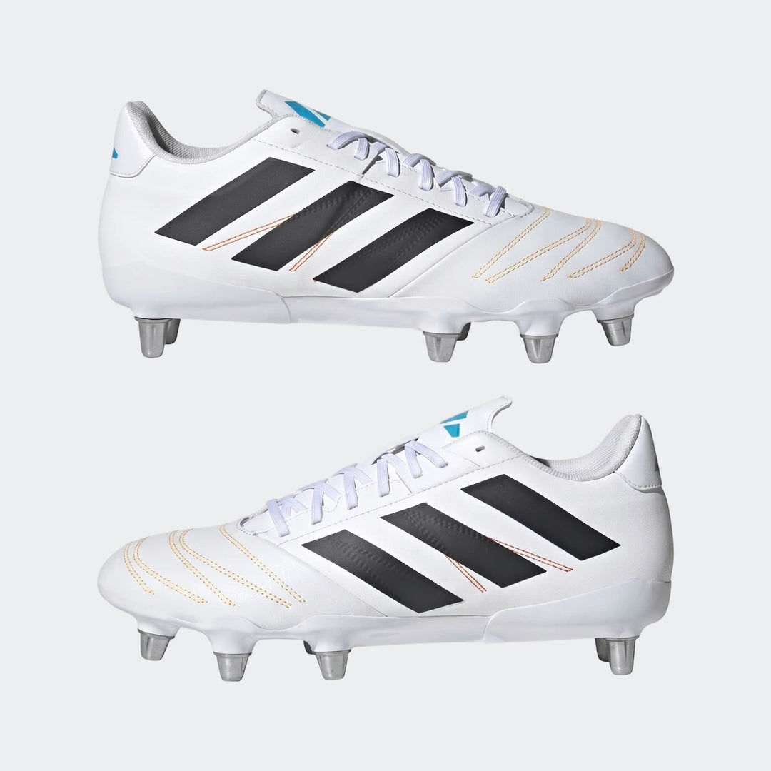 A pair of white Adidas Kakari Elite SG rugby boots with black stripes, orange stitching, and silver studs.