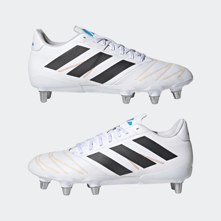 A pair of white Adidas Kakari Elite SG rugby boots with black stripes, orange stitching, and silver studs.