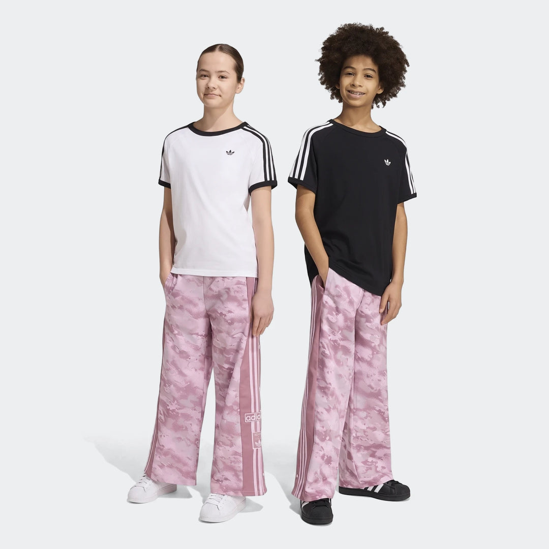 Two young models showcase pink camouflage Adidas Loose Adibreak Camo Twill Trousers, featuring side stripes. One wears a