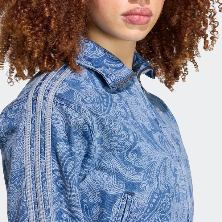 Close-up of a woman wearing an Adidas Liberty London Firebird denim tracktop in blue with an intricate paisley print and