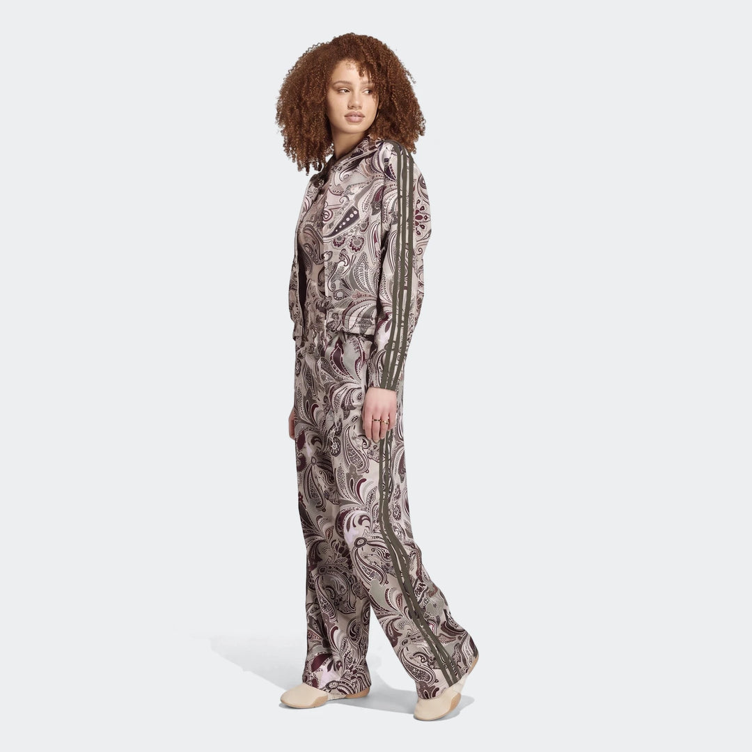 Full-body shot of a model wearing the Adidas Liberty London Firebird Satin Track Top and matching pants, featuring a unique