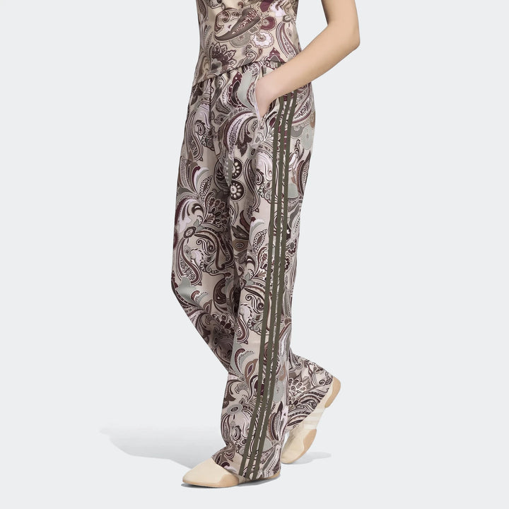 Adidas Liberty London Firebird Satin Trackpant, featuring a brown and cream paisley print with green side stripes, worn by a