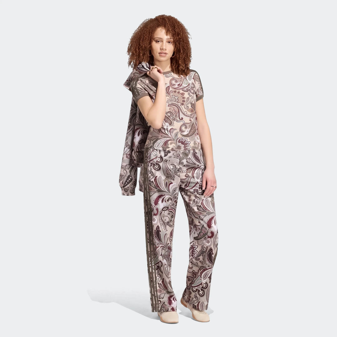 Woman models an Adidas Liberty London Firebird Satin Trackpant and matching top, featuring a unique paisley pattern.
