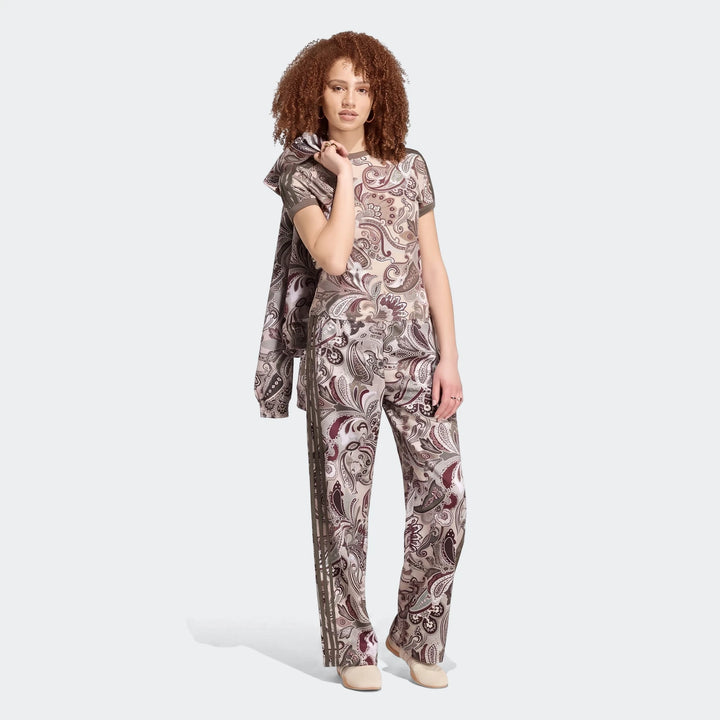 Woman models an Adidas Liberty London Firebird Satin Trackpant and matching top, featuring a unique paisley pattern.