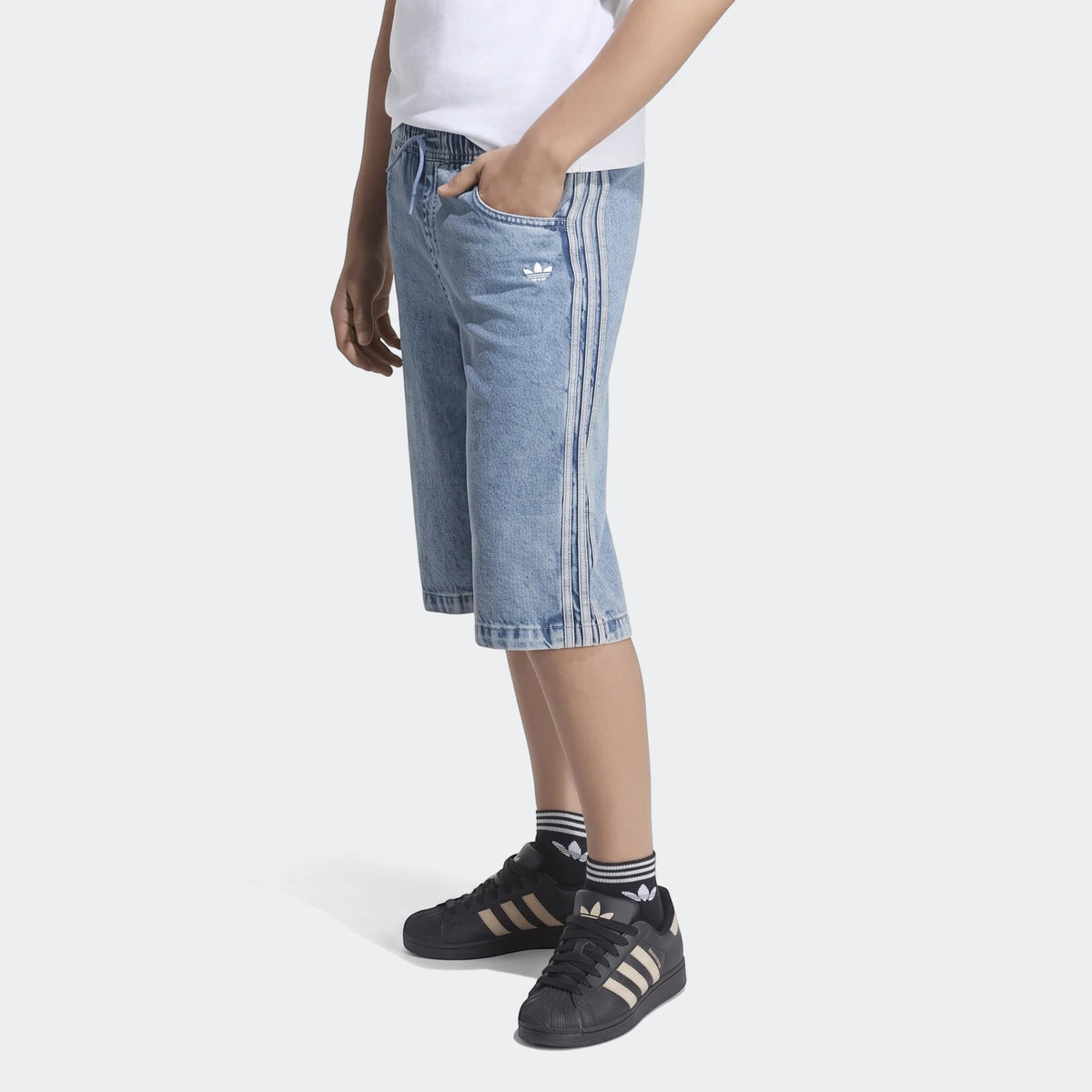 Model in Adidas light blue Loose Denim Jorts with side stripes, white t-shirt, and black sneakers with striped socks, shown