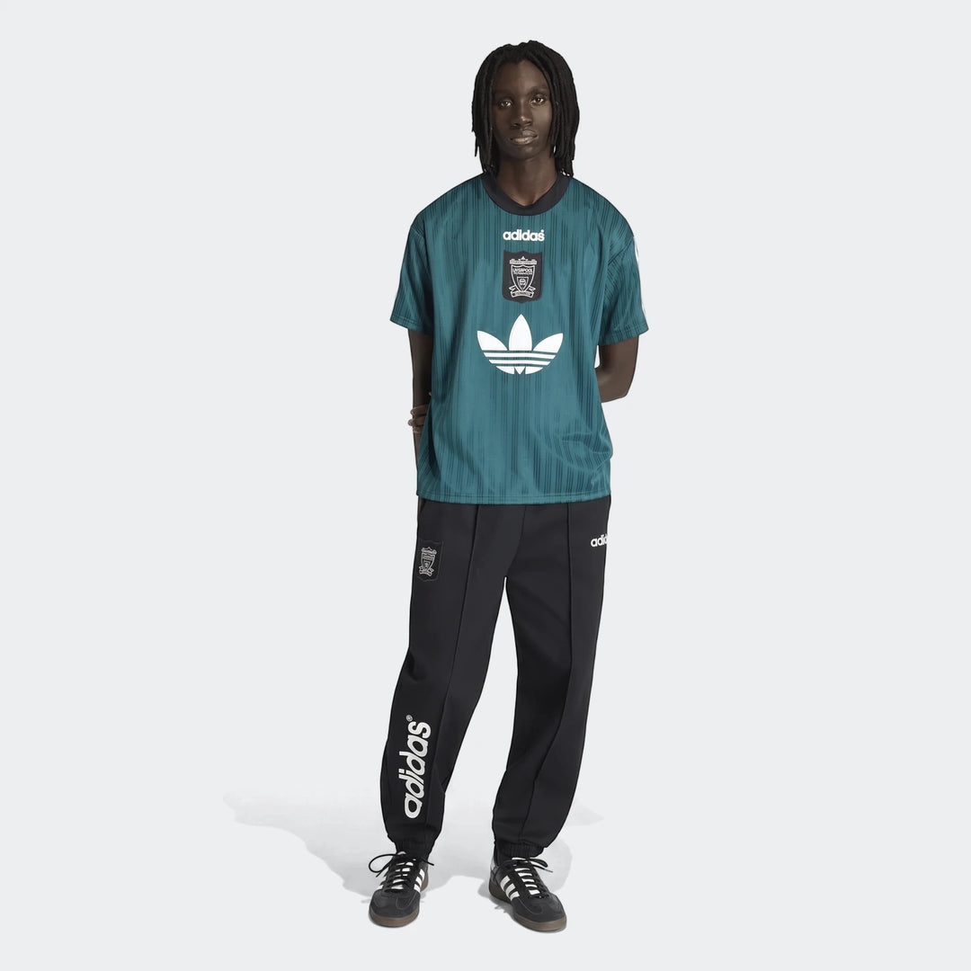 Full shot of a model wearing the green Adidas Liverpool FC 1995 Poly T-Shirt and black track pants.