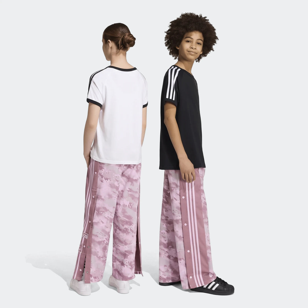Two kids model pink camo Adidas Loose Adibreak Camo Twill Trousers, full length, one facing back in white tee, one smiling