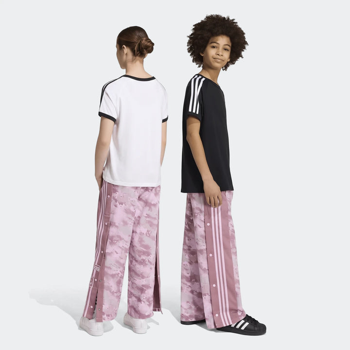 Two kids model pink camo Adidas Loose Adibreak Camo Twill Trousers, full length, one facing back in white tee, one smiling