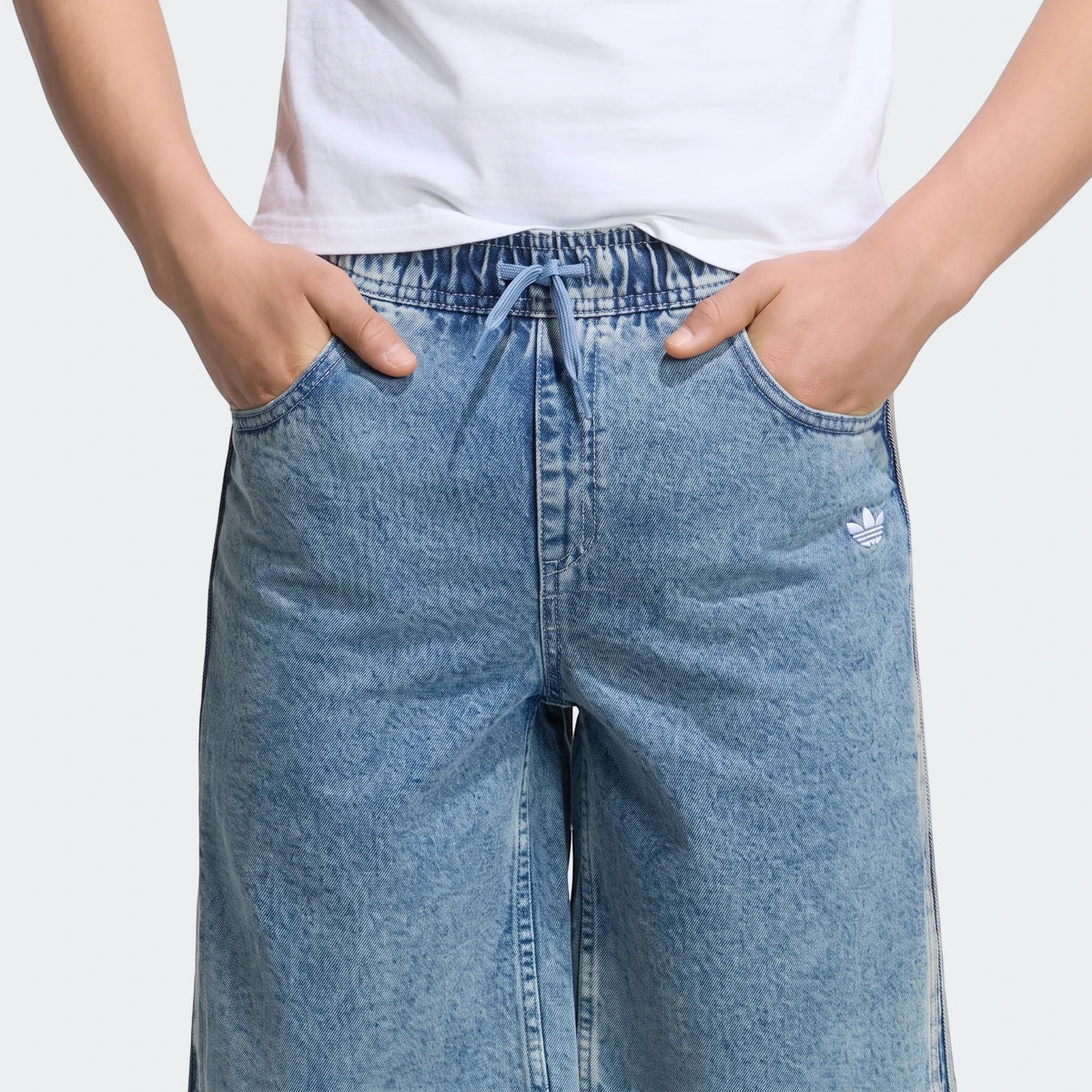 Close-up of a person wearing blue acid wash Adidas Loose Denim Jorts, featuring an elastic drawstring waist and embroidered