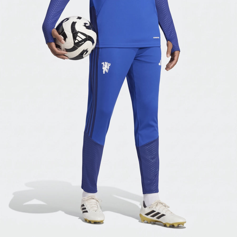 Blue Adidas Manchester United 26/27 Cup Tiro training pants worn by a person holding a soccer ball, paired with white and