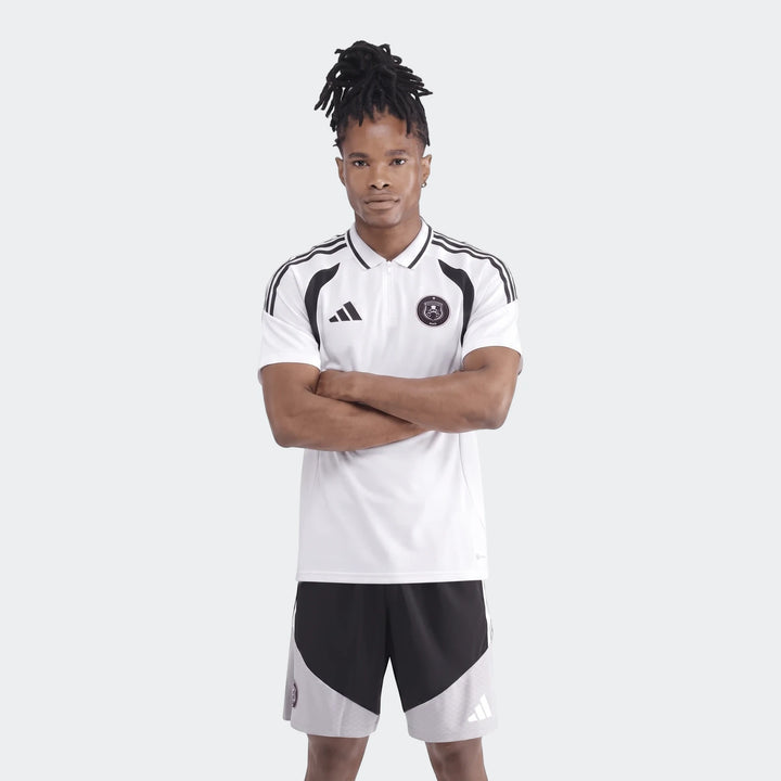 Male model wearing a white Adidas Op Tiro26C Polo shirt with black accents and black and gray shorts, posing with arms