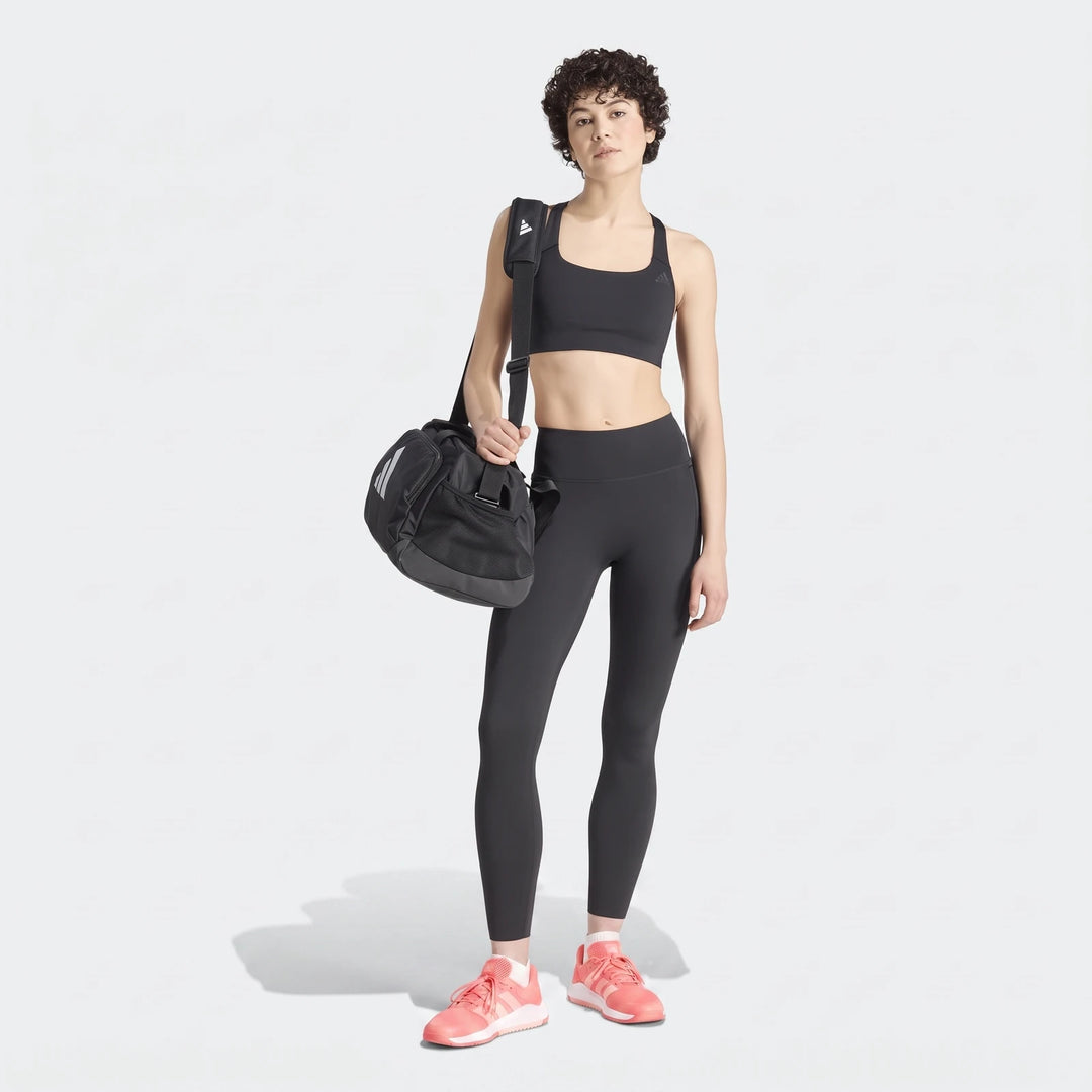 Woman wearing black Adidas Optime Workout Contour full length leggings, a black sports bra, and coral athletic shoes,