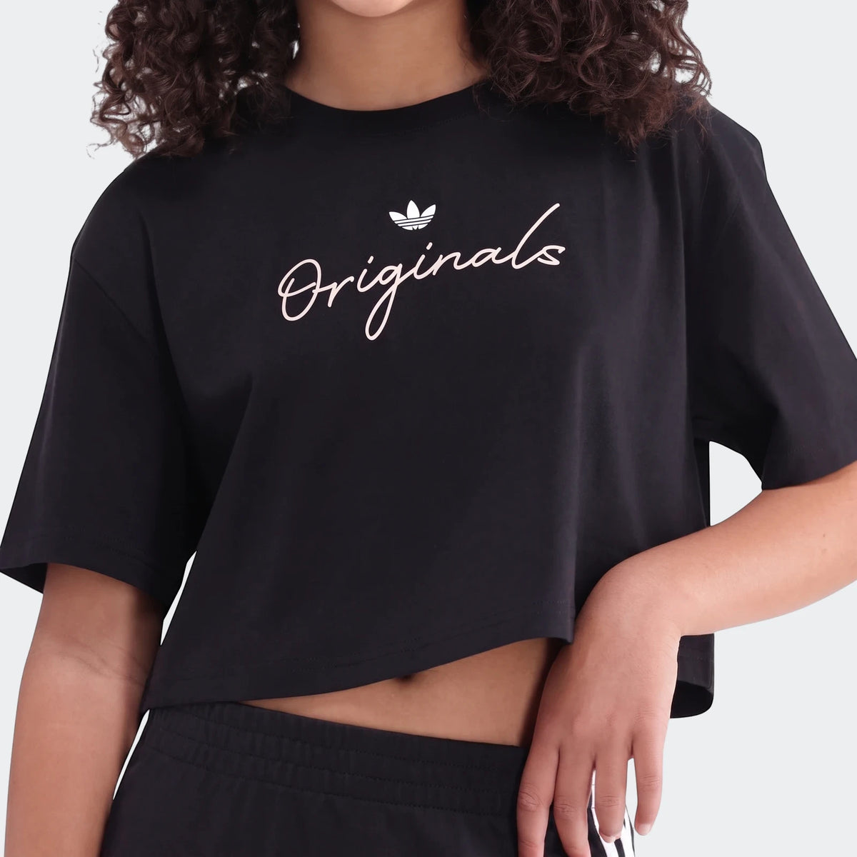 Black Adidas Originals Youth Script Tee worn by a model, featuring a white trefoil logo and 'Originals' script, paired with