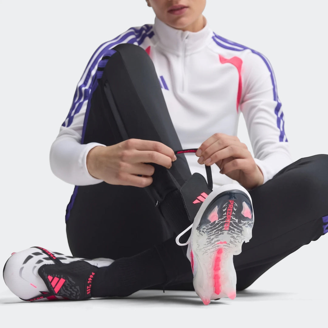 A person sits on the floor, tying the pink laces of white, black, and pink Adidas Predator Elite Fold-Over Tongue Firm