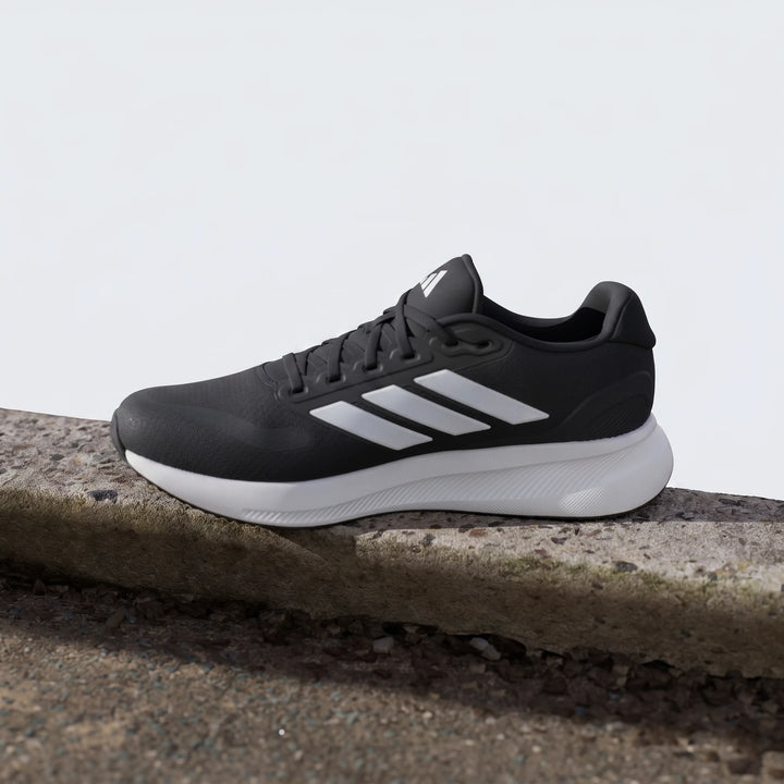 Adidas Runfalcon 5 Black Sneakers with white stripes and a white sole, photographed outdoors on a concrete ledge.
