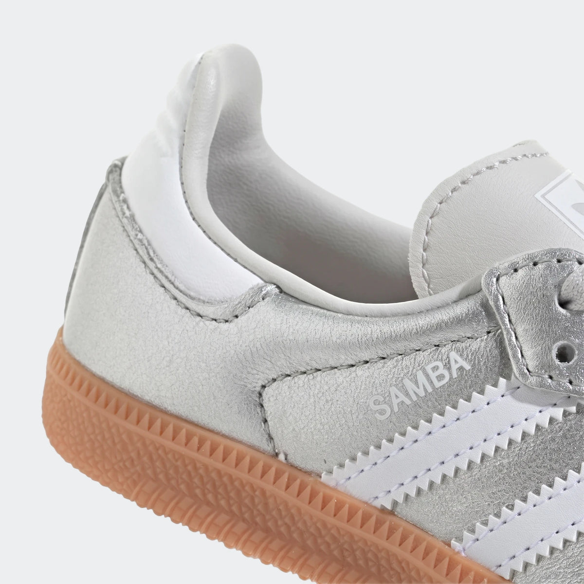Close-up of a silver metallic Adidas Samba Og shoe with white stripes and a gum sole, viewed from the side.