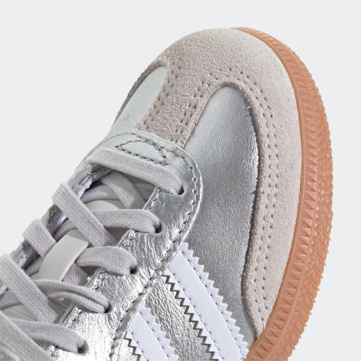 Close-up of a silver metallic and light grey suede Adidas Samba OG shoe with white laces and a gum sole, viewed from the