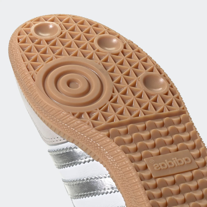 Close-up view of the gum sole and metallic silver and white upper of an Adidas Samba OG shoe, highlighting the traction