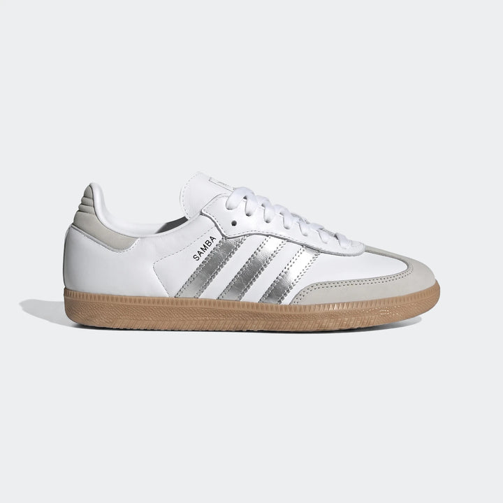 White Adidas Samba Og Shoes with metallic silver stripes and a gum sole, shown in a side view.