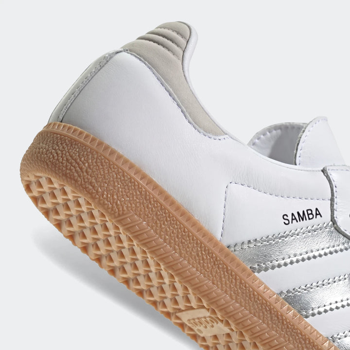 Close-up of Adidas Samba Og shoes, featuring white leather, silver stripes, and a gum sole, viewed from a low angle showing