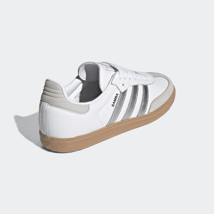 White Adidas Samba Og shoes with metallic silver stripes and a gum sole, viewed from a rear-quarter angle.