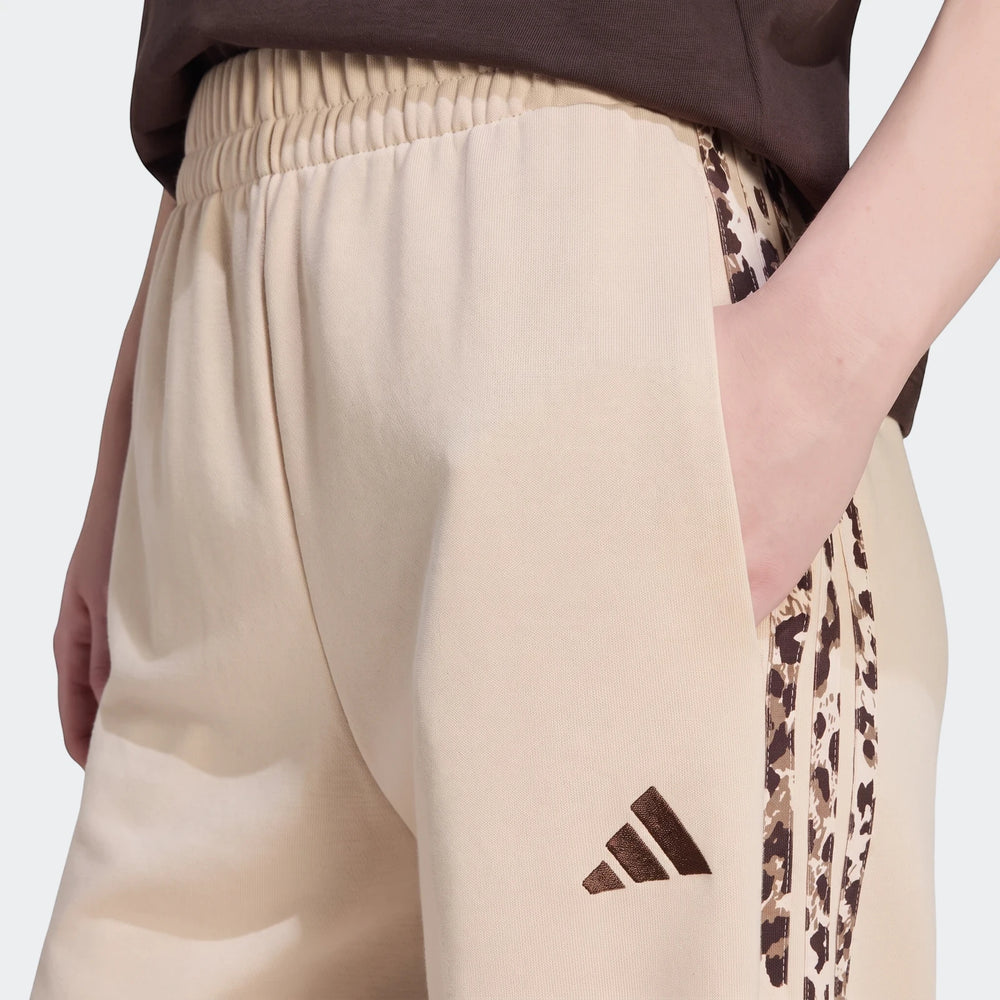 Close-up of beige Adidas Seasonal Essentials Animal Print 3-Stripes Joggers worn by a model, featuring side stripes and a