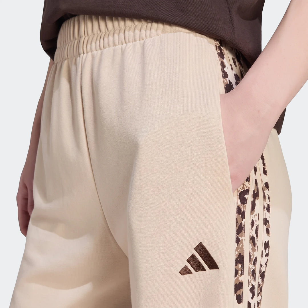 Close-up of beige Adidas Seasonal Essentials Animal Print 3-Stripes Joggers worn by a model, featuring side stripes and a