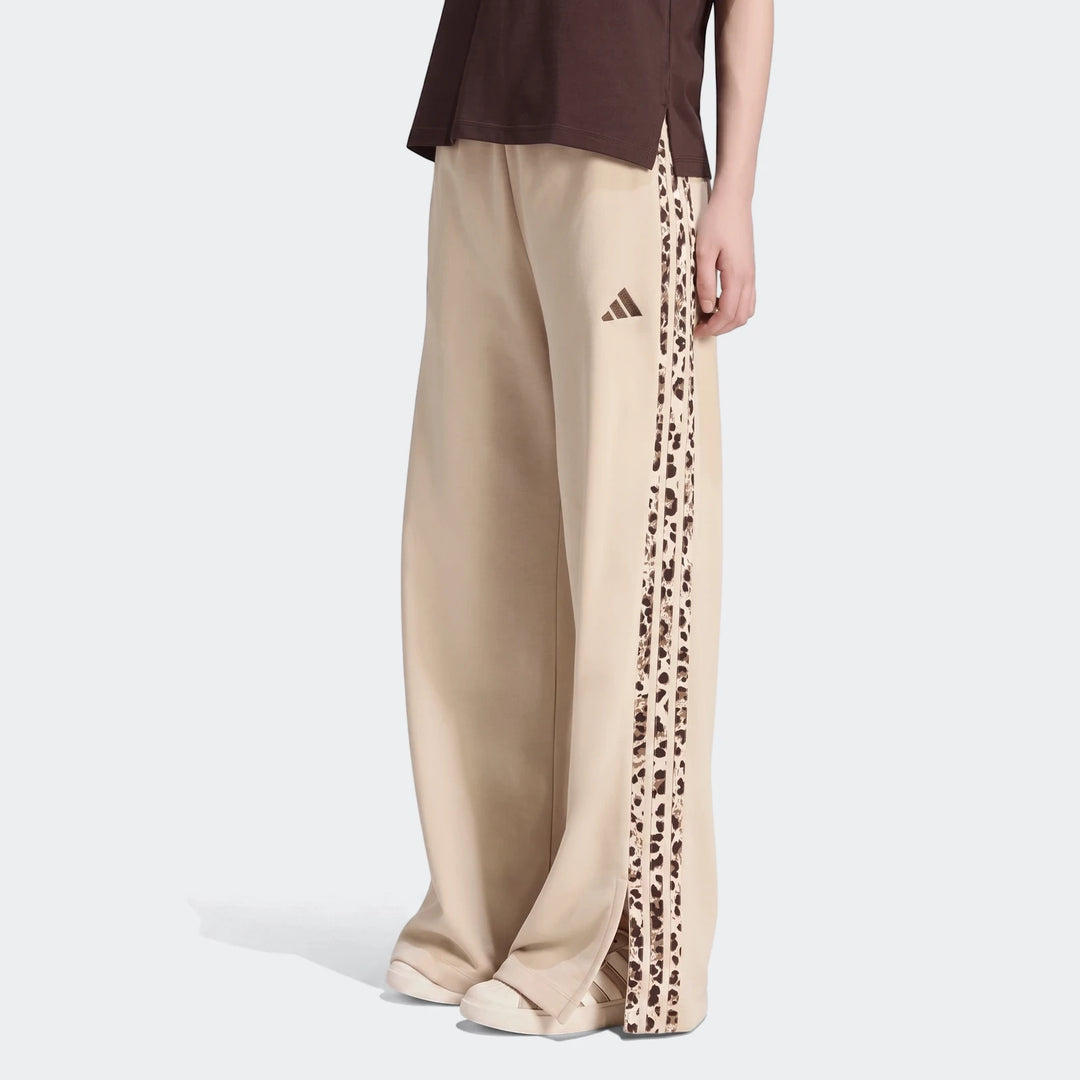 A person wears beige Adidas Seasonal Essentials Animal Print 3-Stripes wide-leg joggers, featuring leopard print stripes