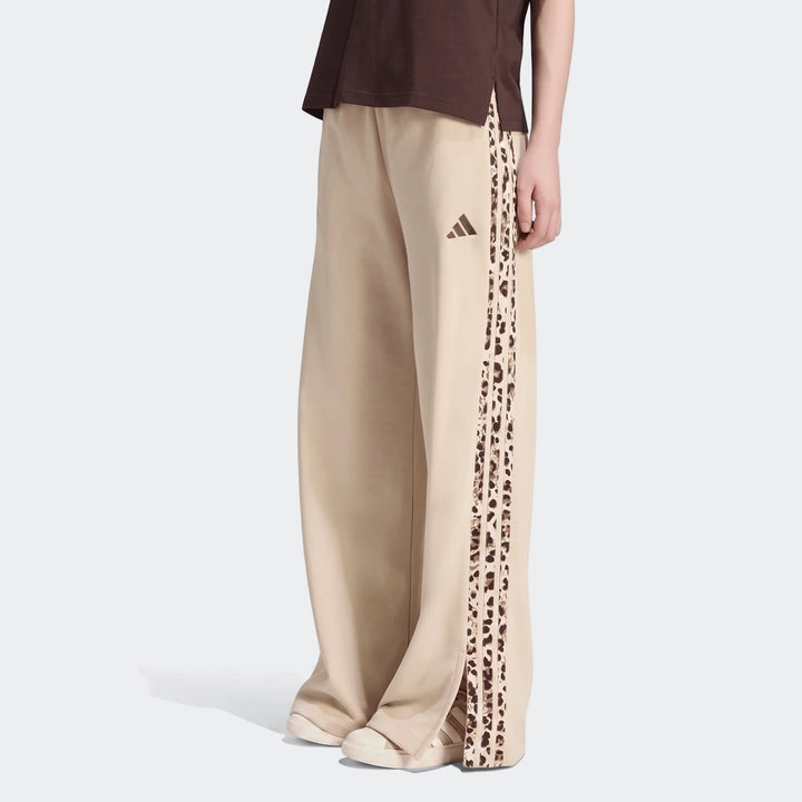 A person wears beige Adidas Seasonal Essentials Animal Print 3-Stripes wide-leg joggers, featuring leopard print stripes