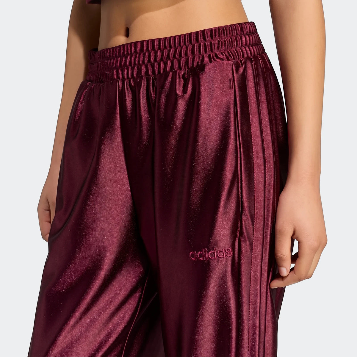 Close-up of maroon Adidas Seasonal Essentials Satin Tracksuit Bottoms with an elasticated waist and subtle embroidered logo.