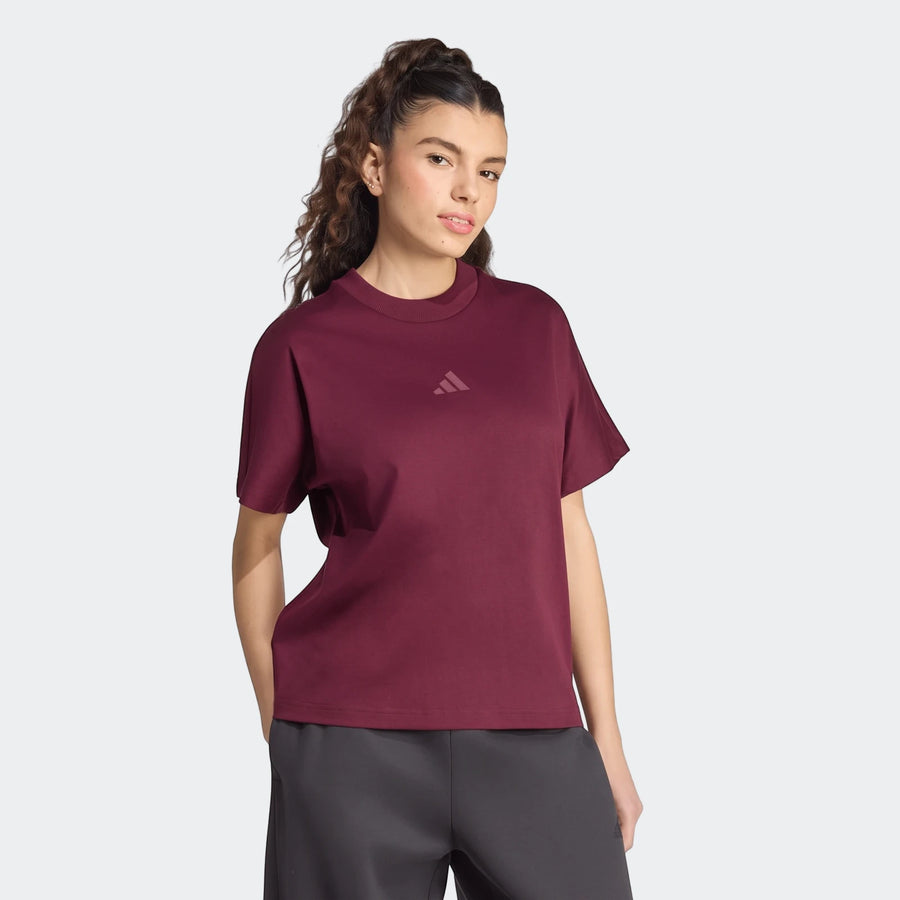 A woman models a maroon Adidas Soft Lux Loose T-Shirt, a comfortable and stylish short-sleeved top, paired with dark pants,