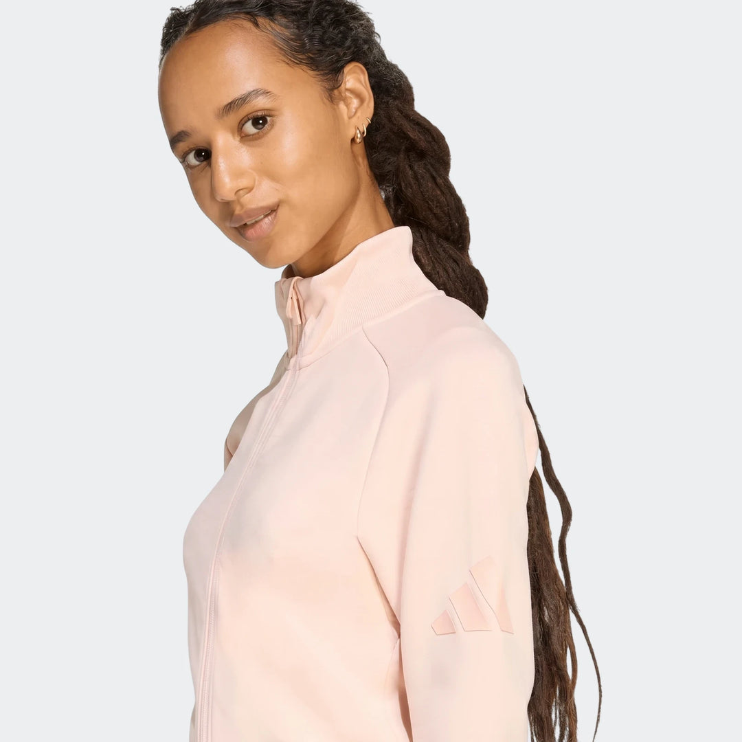 Light pink Adidas Soft Luxe Slim Track Top worn by a model. Features a high collar and subtle Adidas logo on the sleeve.
