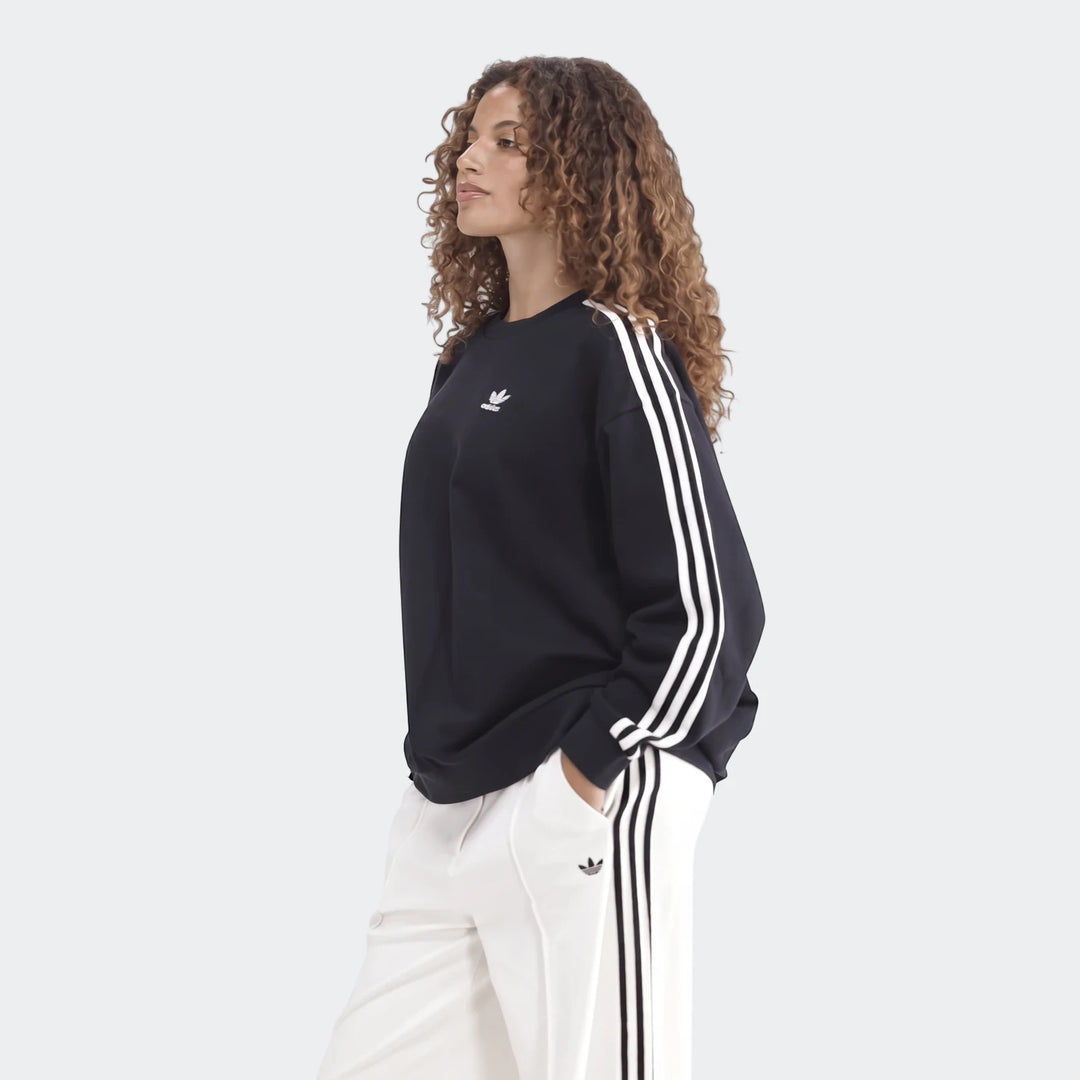 Woman wearing a black Adidas Sportswear 3-Stripes Oversized Crew Sweatshirt and white track pants, posing with hands in