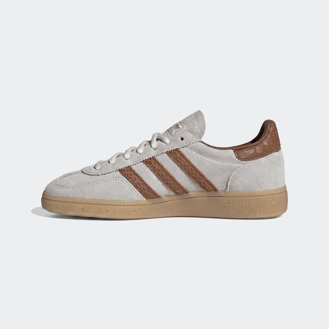 Side view of a light gray suede Adidas sneaker with brown stripes, textured brown heel accent, and a gum sole.