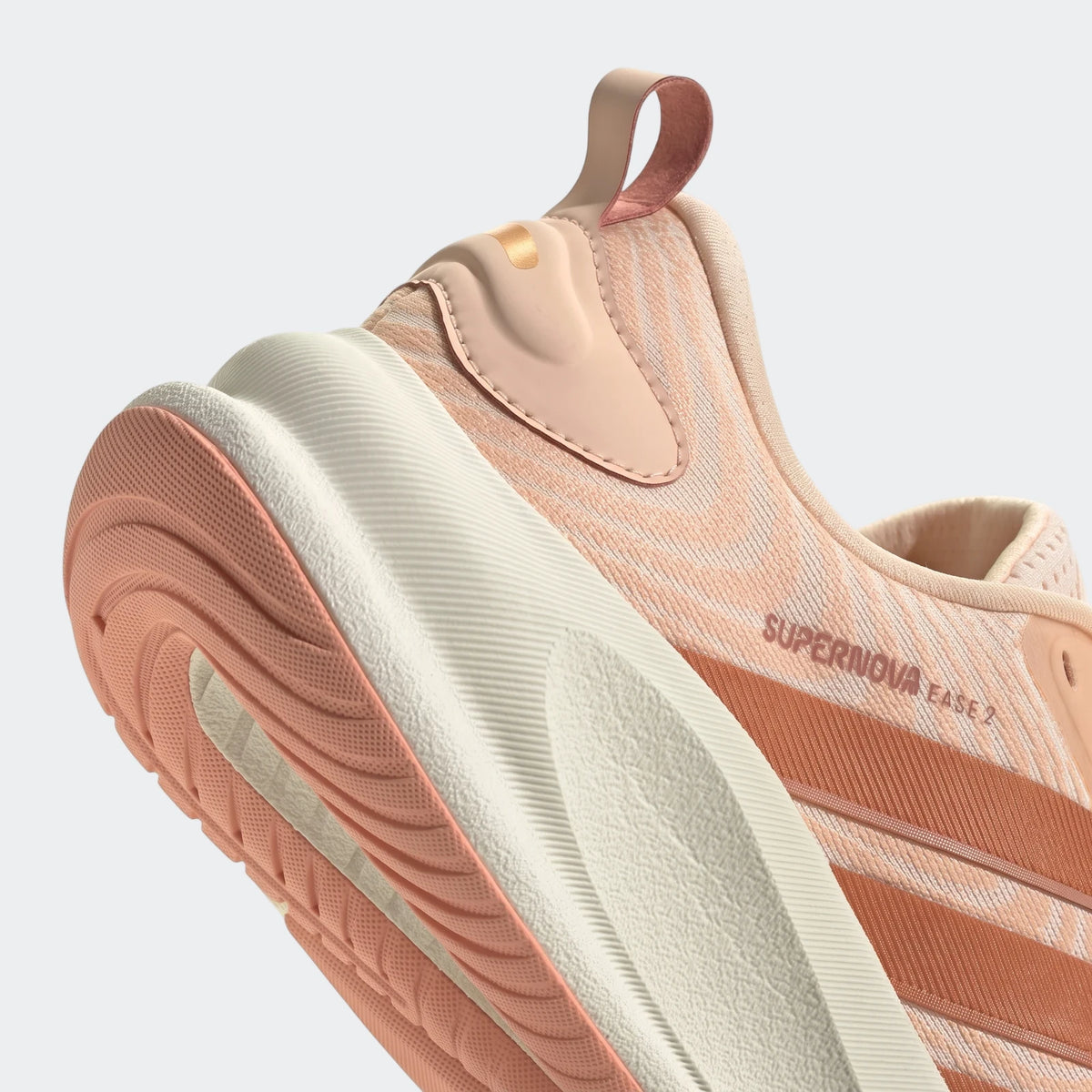 Close-up of the rear and side of an Adidas Supernova Ease 2 running shoe in a peach and off-white colorway, highlighting the