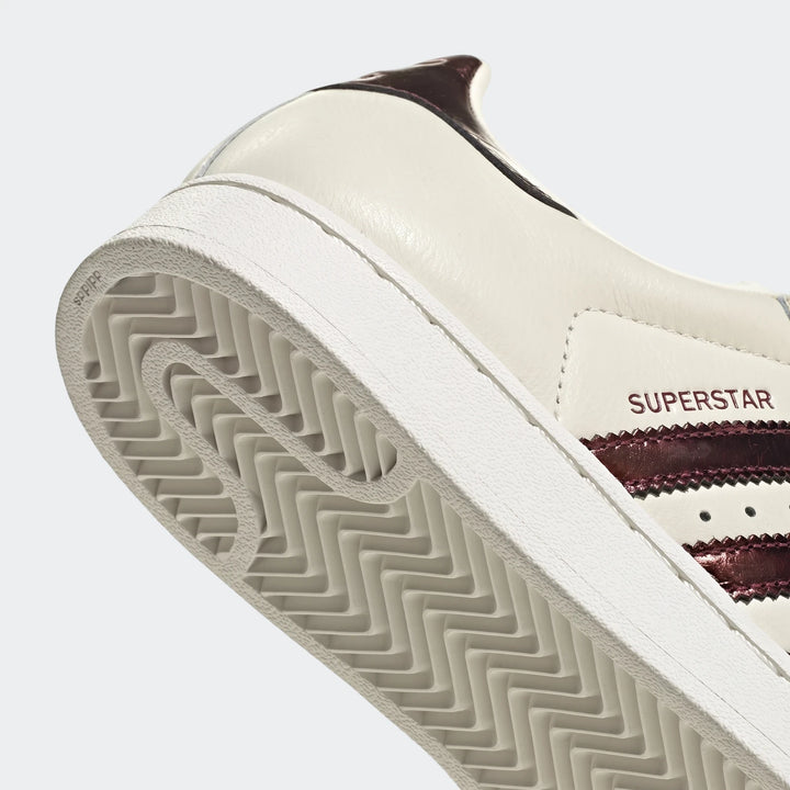 Close-up of an Adidas Superstar II shoe in creamy white leather with metallic brown stripes, showcasing the outsole.